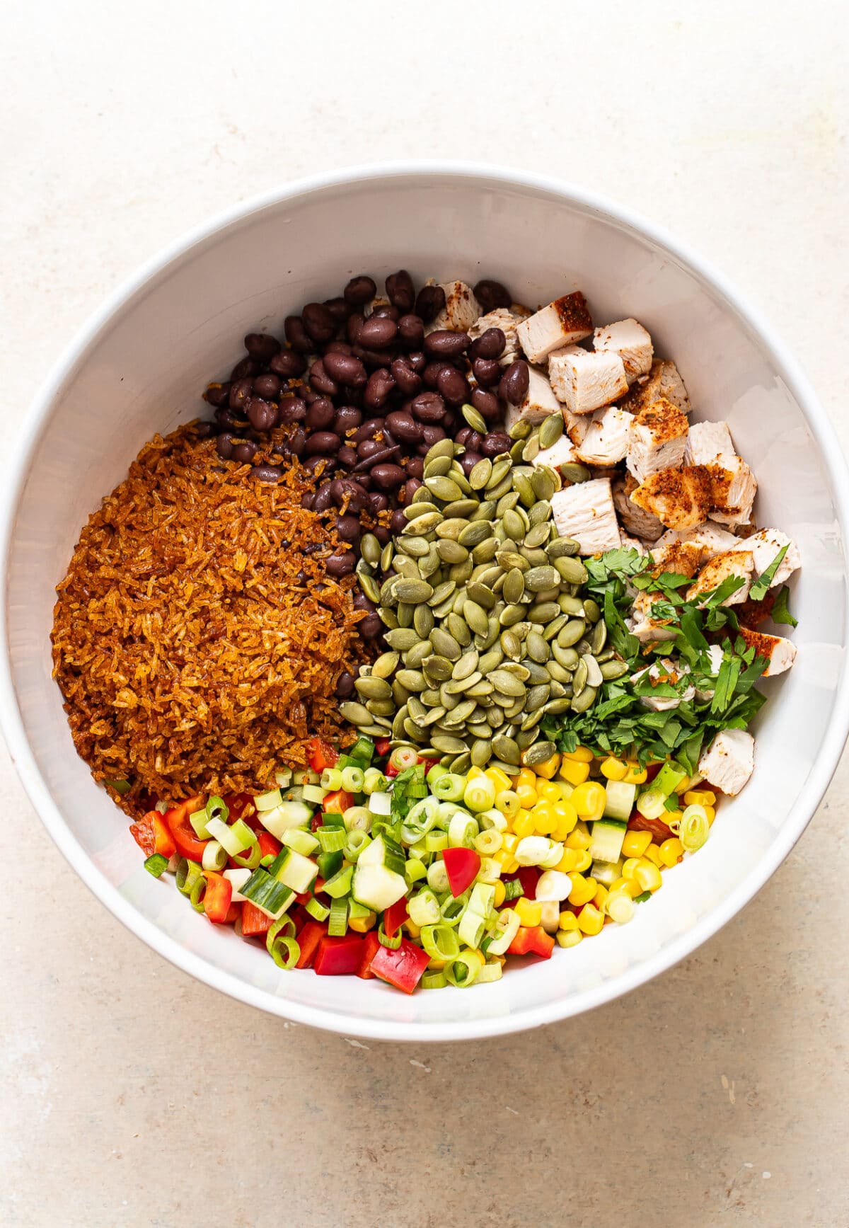 Crispy rice, diced chicken, black beans, corn, peppers, pepitas and green onions in a mixing bowl before being tossed together.