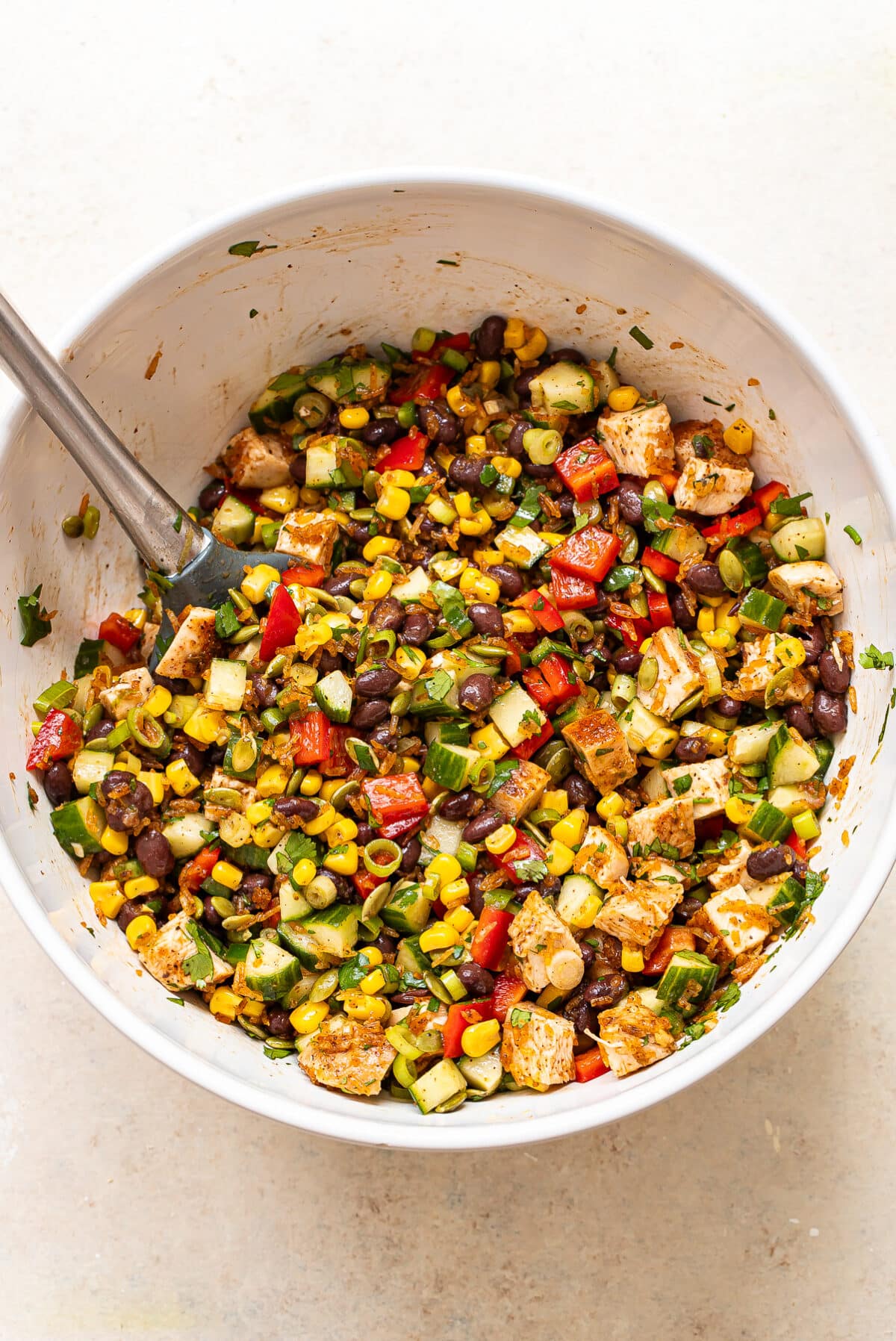 Crispy rice, diced chicken, black beans, corn, peppers, pepitas and green onions in a mixing bowl.