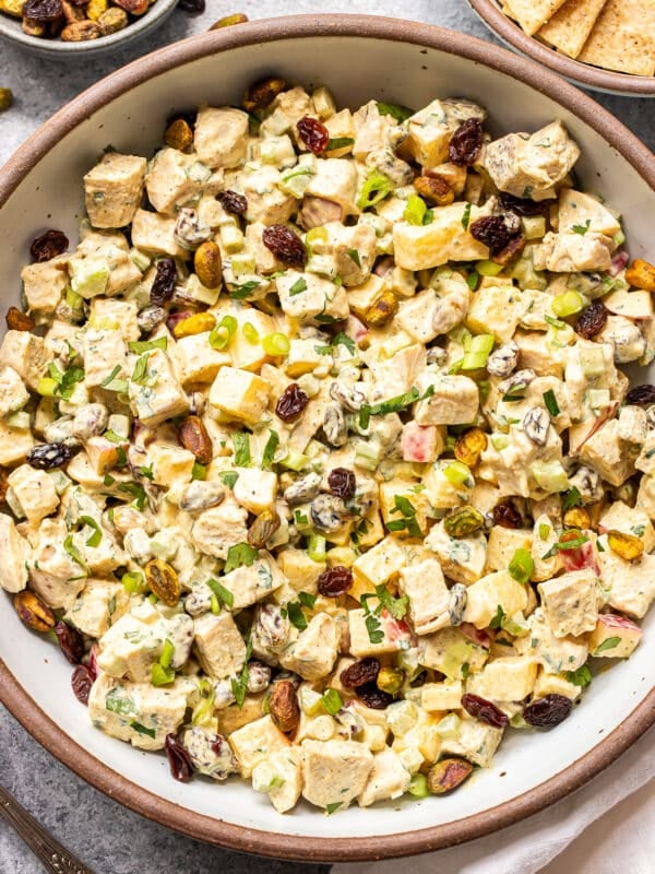 A bowl of creamy Curry Chicken Salad-inspired salad with diced tofu, raisins, pistachios, chopped herbs, and green onions, served with crackers on the side.