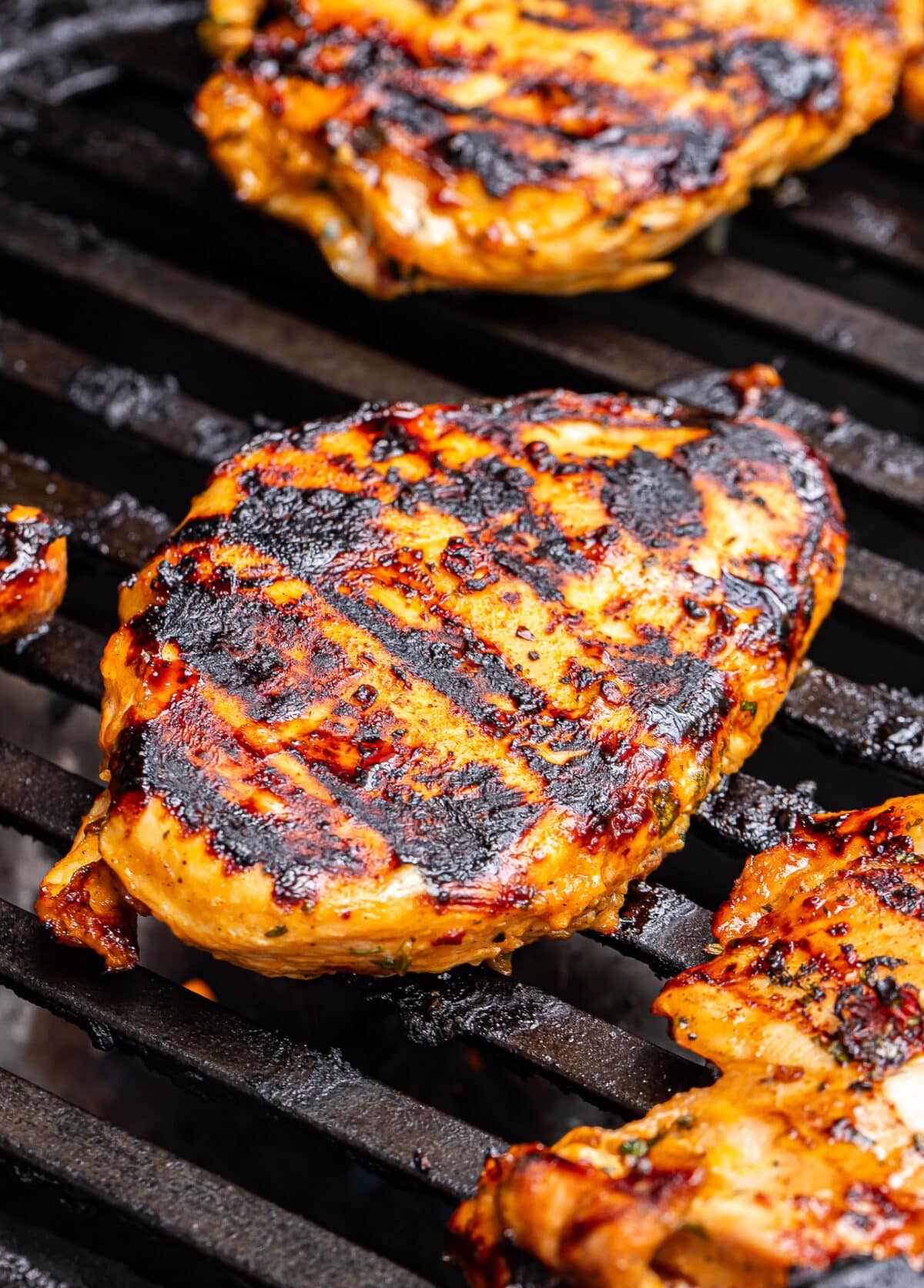 Honey Chipotle Chicken sizzles on the barbecue grill, with grilled chicken breast boasting char marks and a glossy honey chipotle glaze, resulting in a golden brown and slightly charred surface.