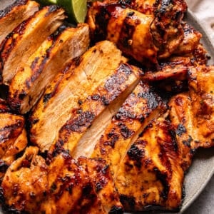 Grilled, sliced Honey Chipotle Chicken breasts with a golden, slightly charred exterior, served on a gray plate with lime wedges and a white napkin in the background.