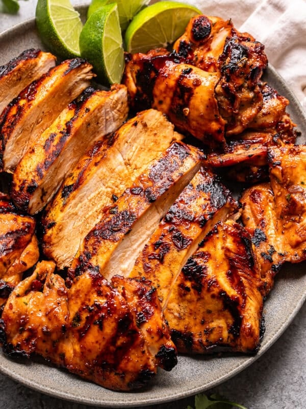 Grilled, sliced Honey Chipotle Chicken breasts with a golden, slightly charred exterior, served on a gray plate with lime wedges and a white napkin in the background.