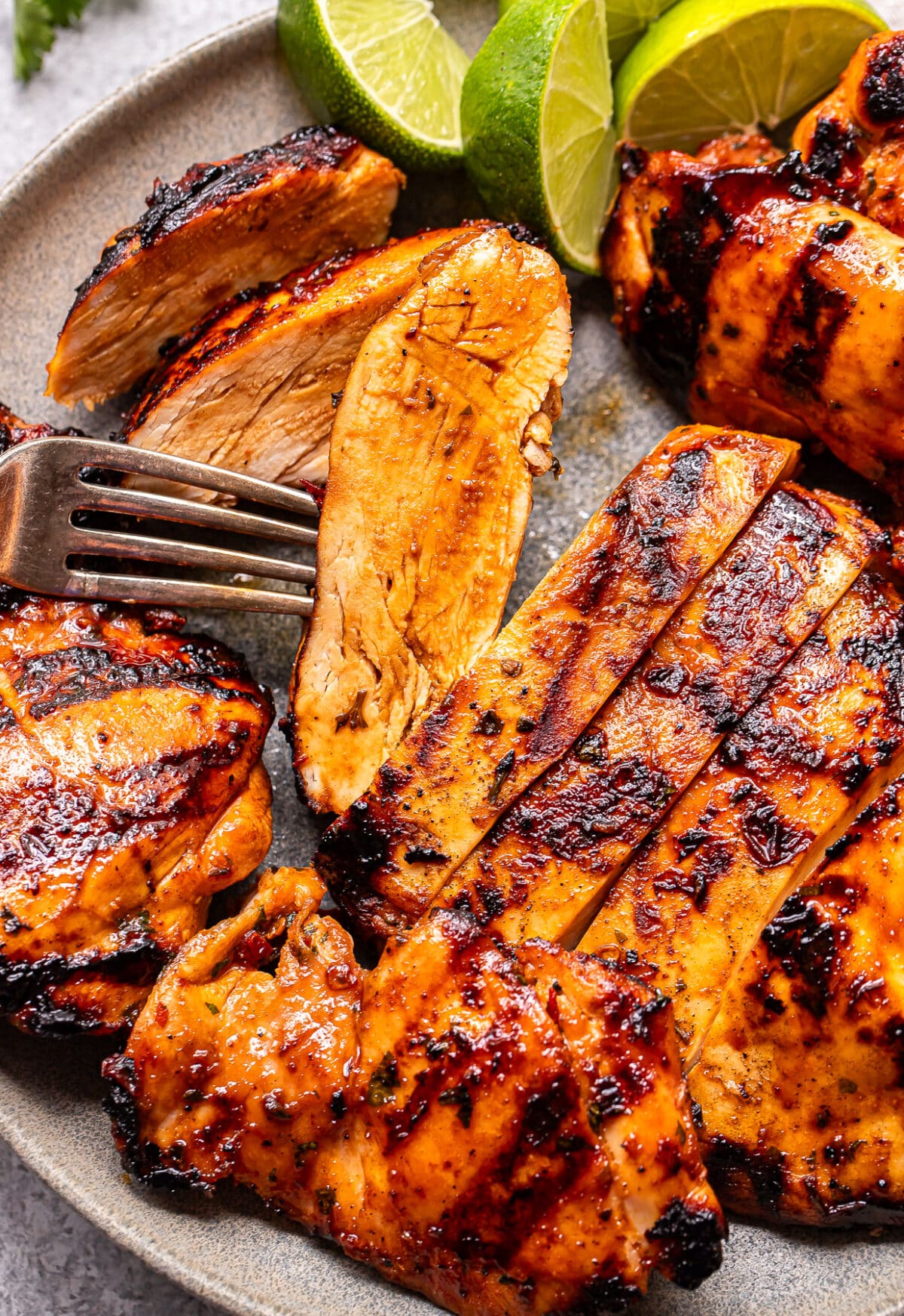 Honey Chipotle Chicken breasts, grilled to golden-brown perfection and sliced on a plate with a fork, garnished with lime wedges. The chicken has a delicious charred appearance and looks juicy and tender.