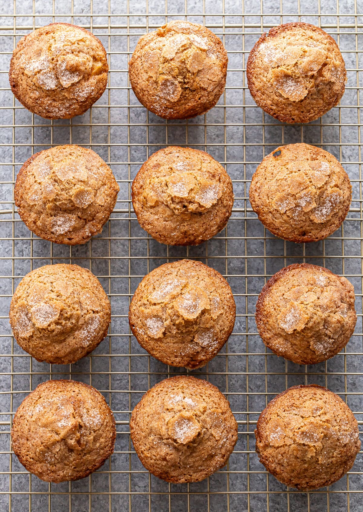 Twelve golden brown Apple Cinnamon Muffins topped with sugar are arranged in neat rows on a wire cooling rack.