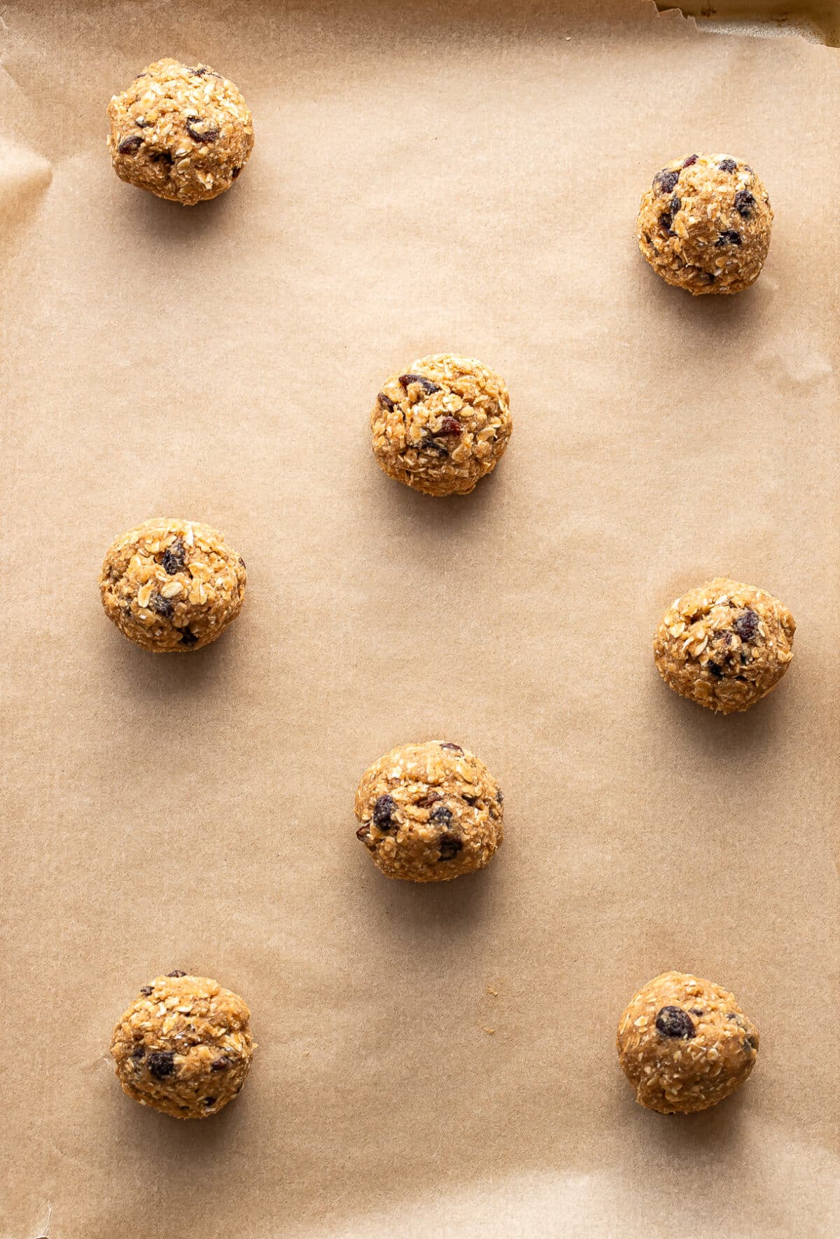Nine oatmeal raisin cookie dough balls are evenly spaced on a baking sheet lined with parchment paper, ready to be baked.