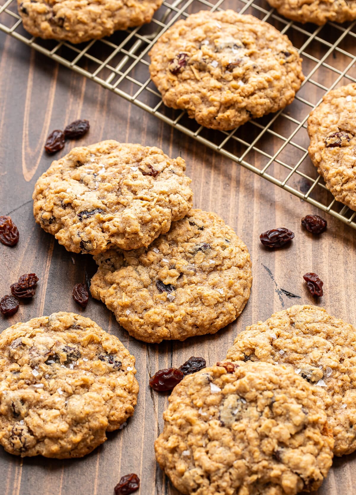 Oatmeal raisin cookies on a wooden surface, with some cookies on a cooling rack and a few raisins scattered around.