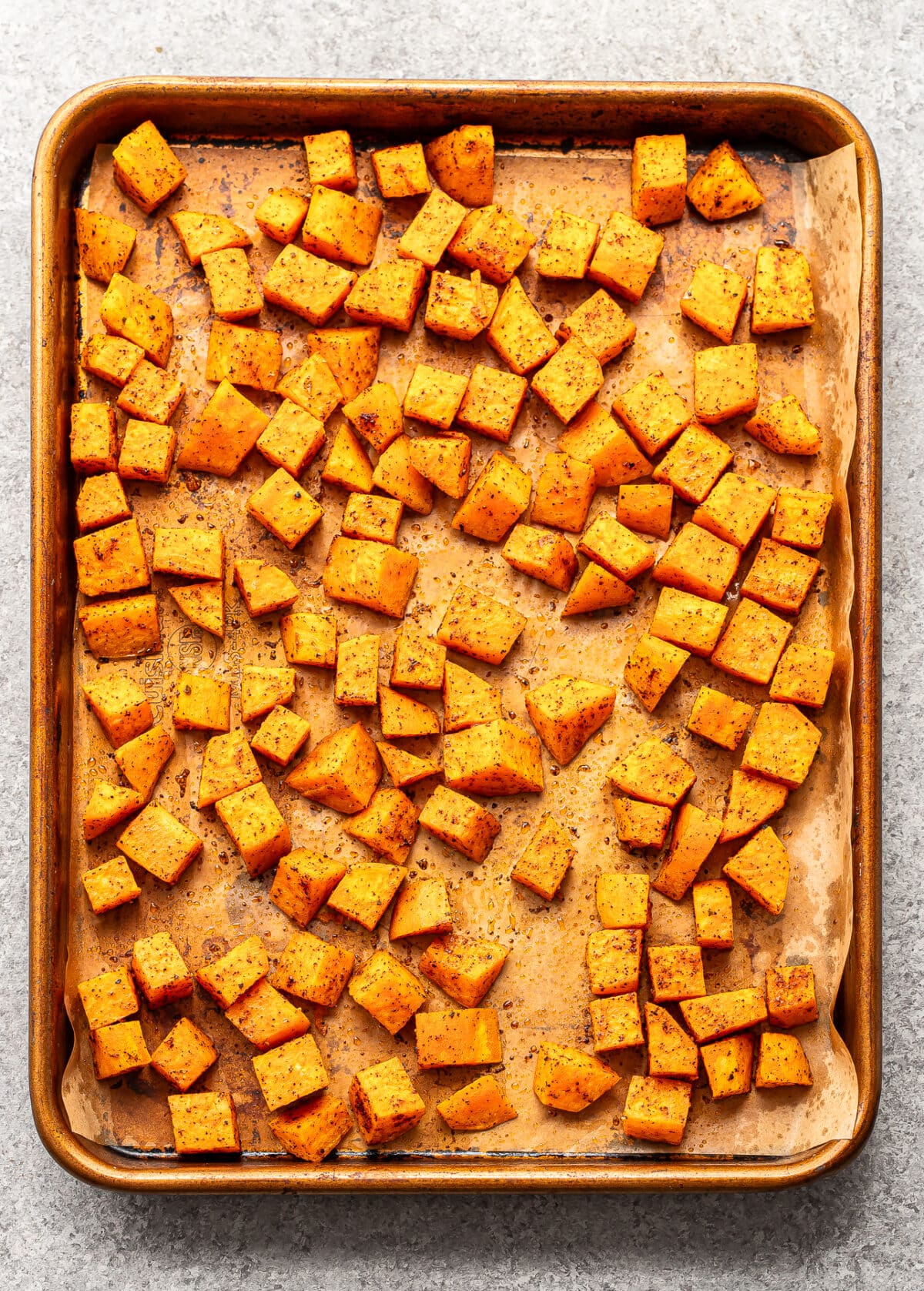 Cubed butternut squash seasoned with spices, spread evenly on a parchment-lined baking sheet, ready for roasting.