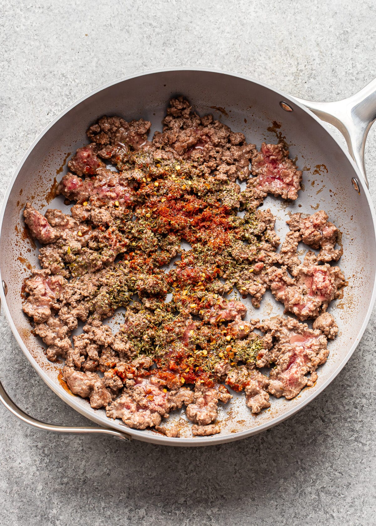 Ground beef and butternut squash browning in a skillet, seasoned with dried herbs and red chili flakes.