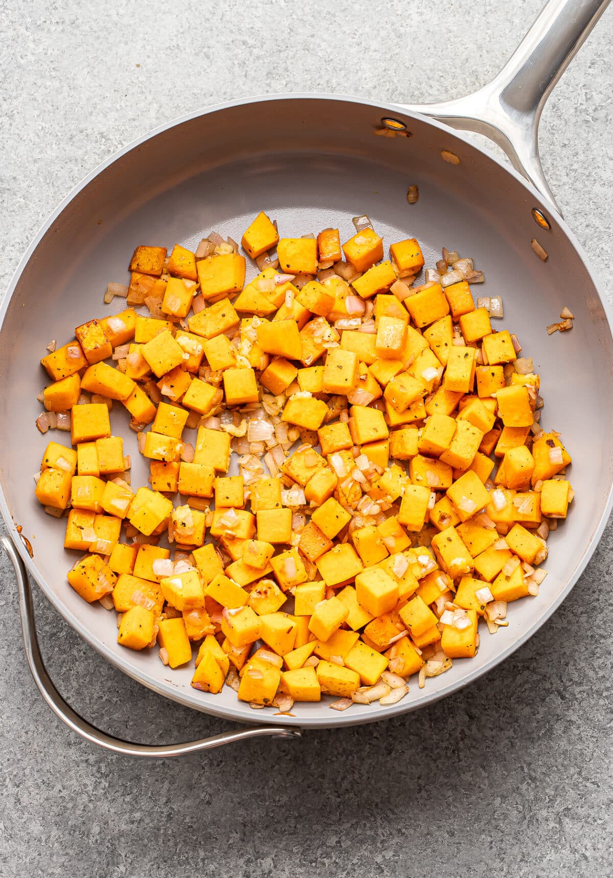 Ground beef, diced butternut squash, and onions sautéing in a gray skillet.