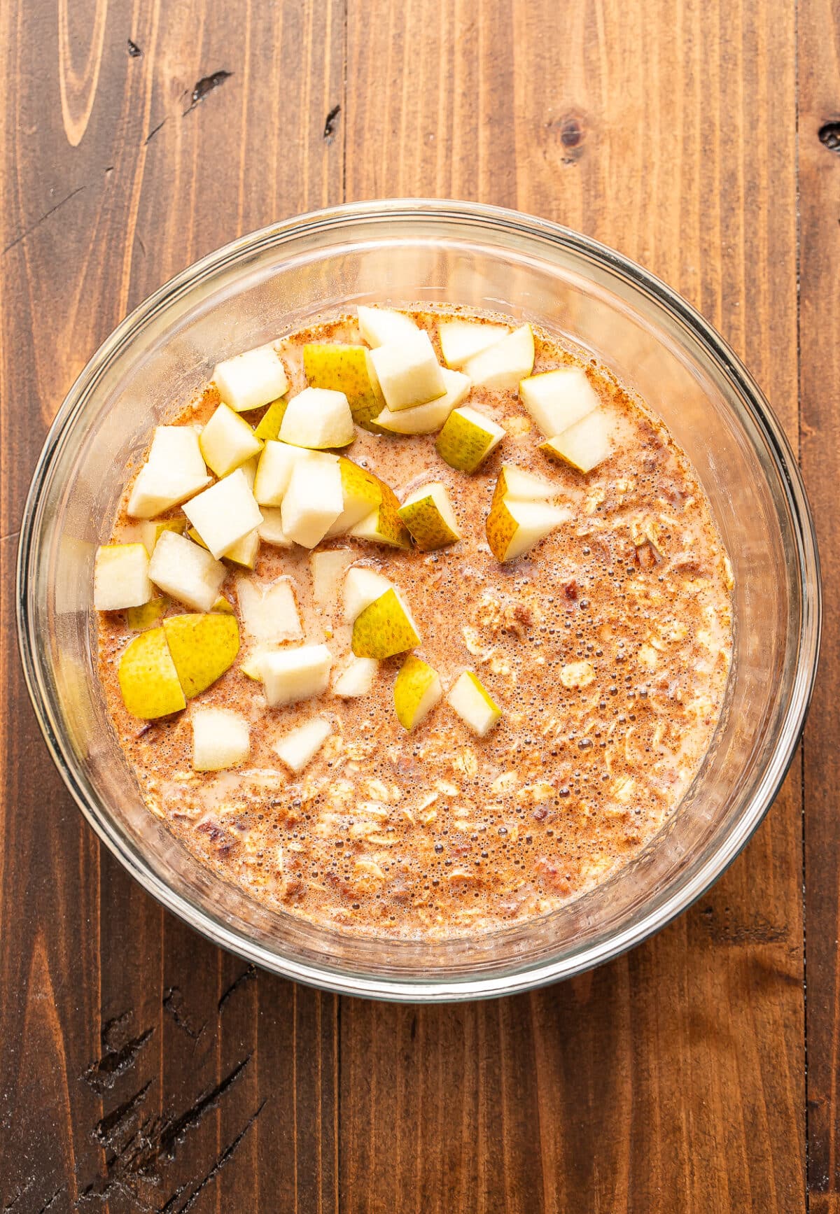 A glass bowl of pear baked oatmeal mixed with milk and cinnamon, topped with diced fresh pears.