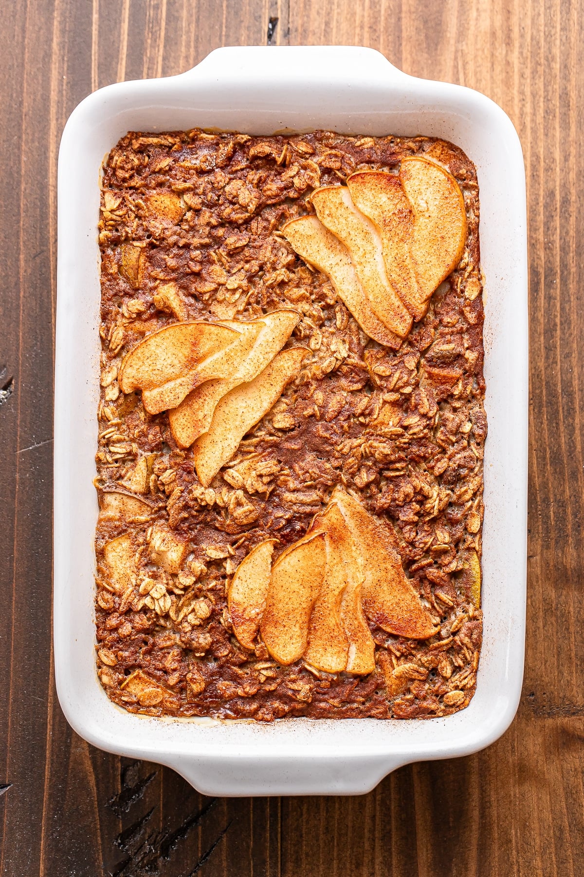 Pear baked oatmeal in a white ceramic baking dish, topped with thin slices of pear.