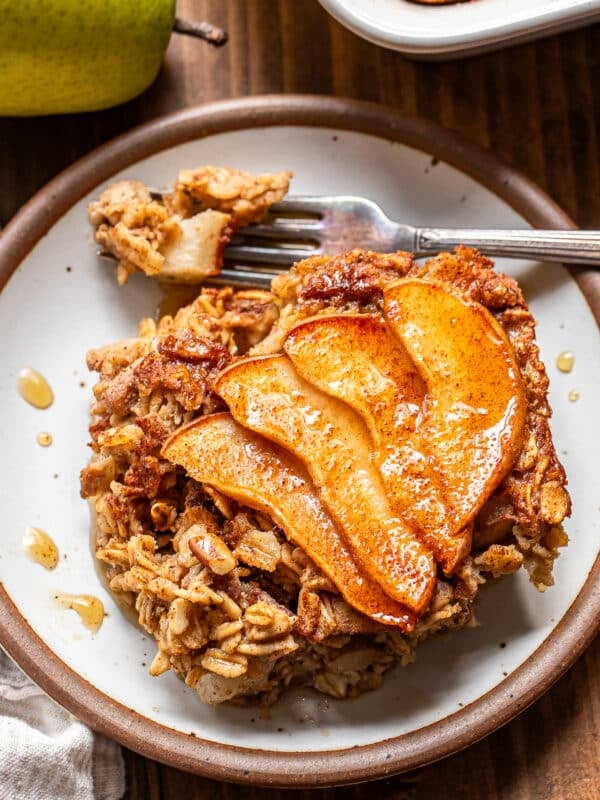 A serving of pear baked oatmeal topped with cinnamon-spiced apple slices on a small plate, with a fork lifting a piece.