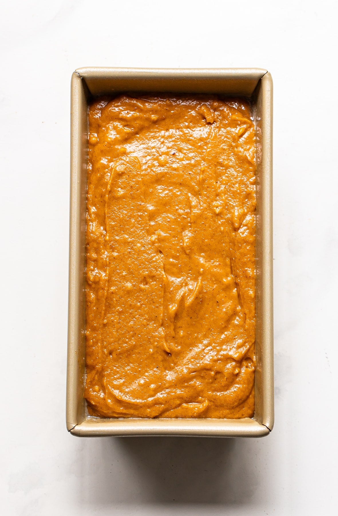 Pumpkin bread batter smoothed into a rectangular metal loaf pan.