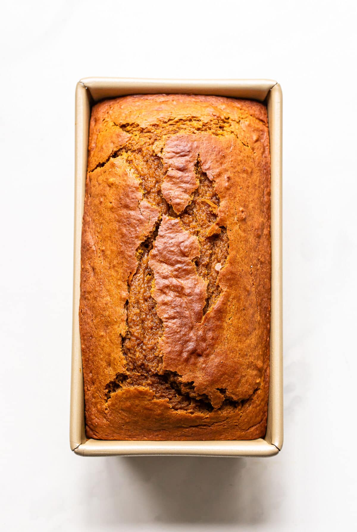 A loaf of golden-brown pumpkin bread baked in a rectangular pan.