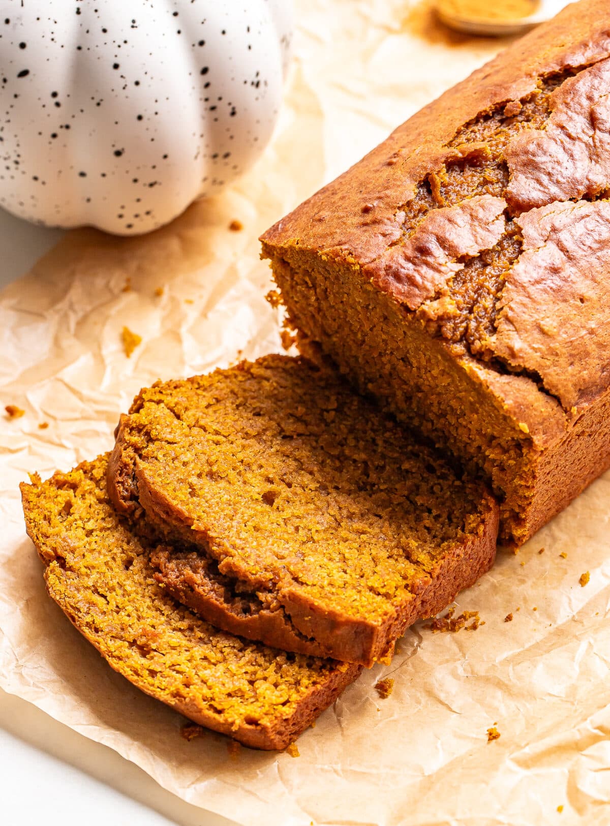 A loaf of sliced pumpkin bread on parchment paper next to a ceramic pumpkin decoration.