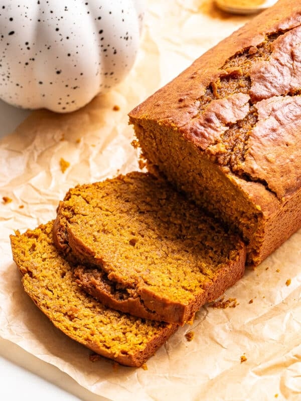A loaf of sliced pumpkin bread on parchment paper next to a ceramic pumpkin decoration.