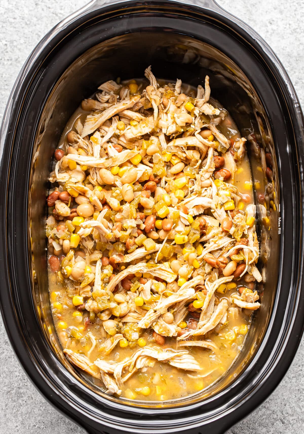 Slow cooker filled with shredded chicken, beans, corn, and green chiles in a savory broth.