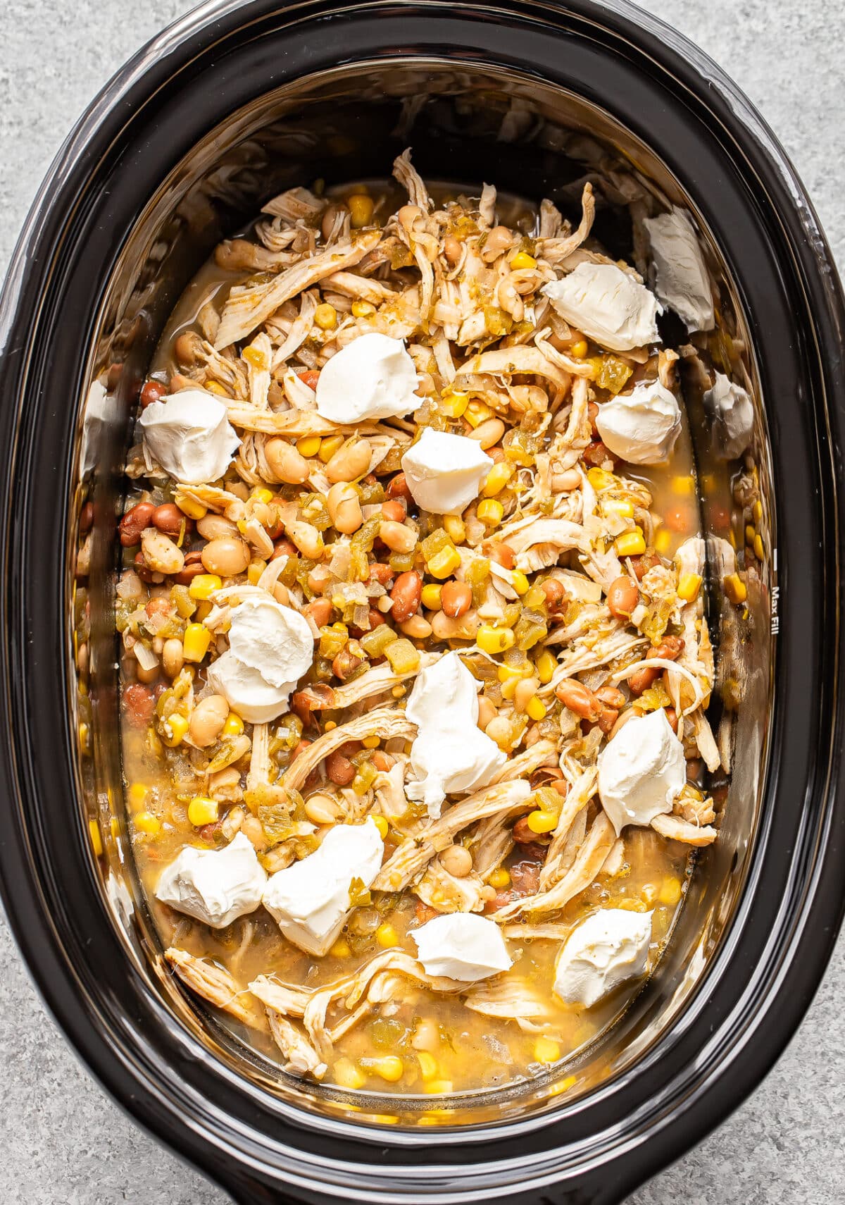 Shredded chicken, beans, corn, and green chiles with dollops of cream cheese in a slow cooker.