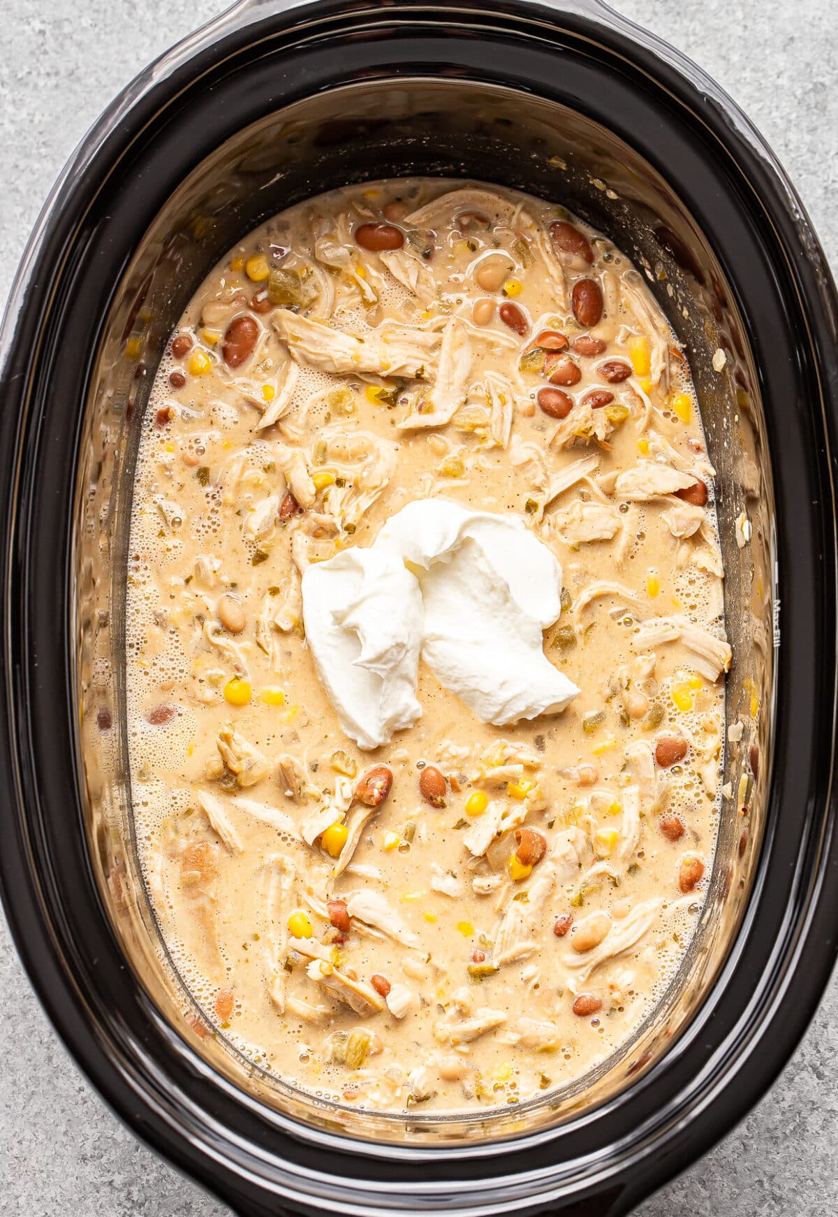 Creamy chicken chili with beans and corn in a slow cooker, topped with a dollop of sour cream.